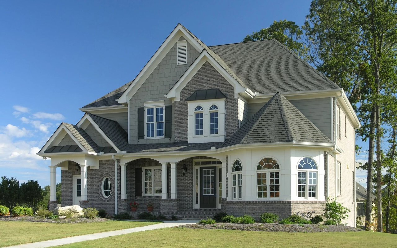 Two-story gray and brick house with multiple gables, arched windows, and a covered front porch.