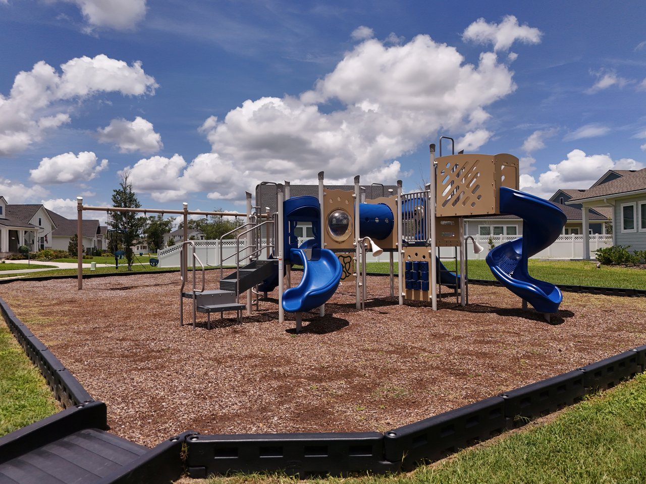 Neighborhood playground with blue slides and climbing equipment in front of nearby homes.