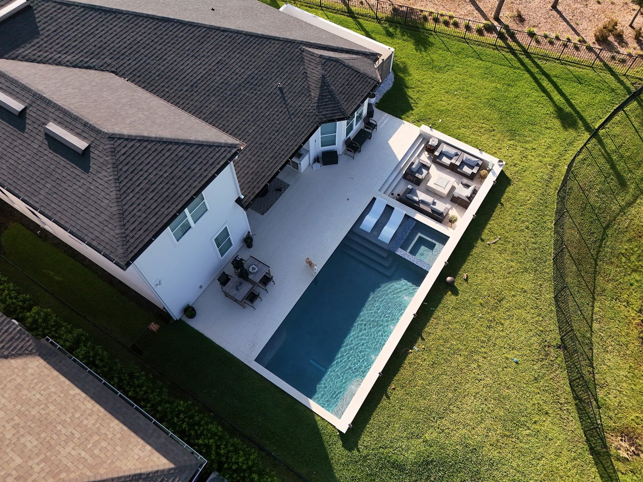 Aerial view of a home with a rectangular pool and furnished patio in a fenced backyard.