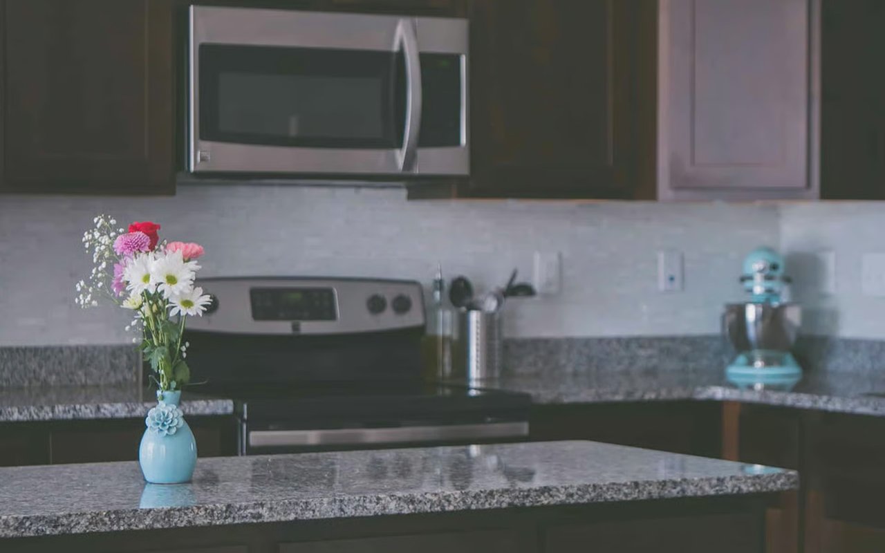 Kitchen with granite island, dark cabinets, turquoise mixer, and flowers in a blue vase.
