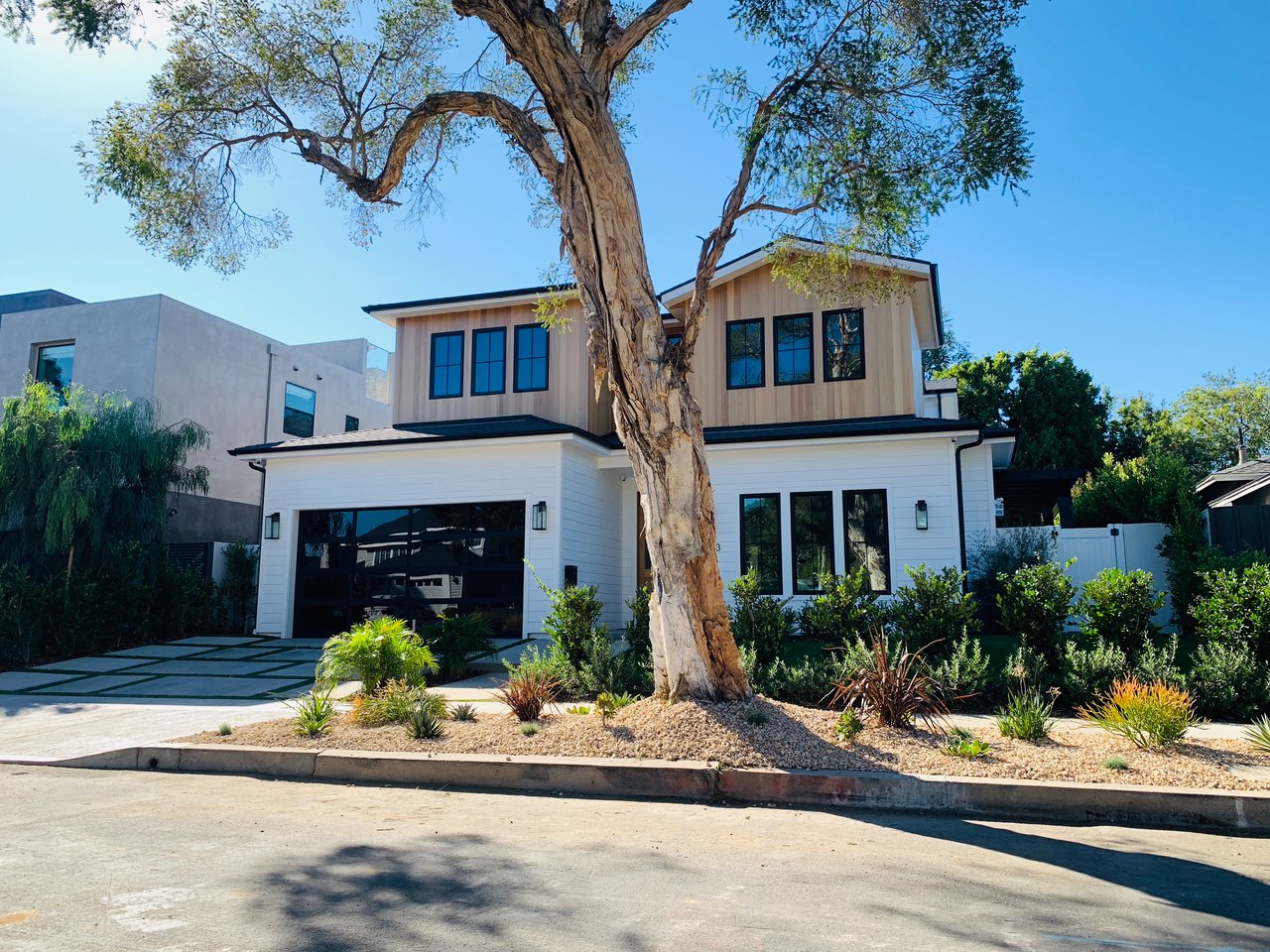 Modern two-story house with white exterior, large shade tree, landscaped front yard, and wide garage.