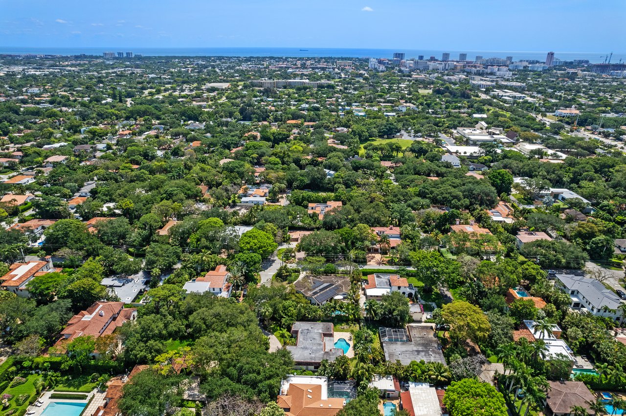 Aerial view of a leafy Boca Raton neighborhood, with homes, a pool, and the ocean on the horizon.