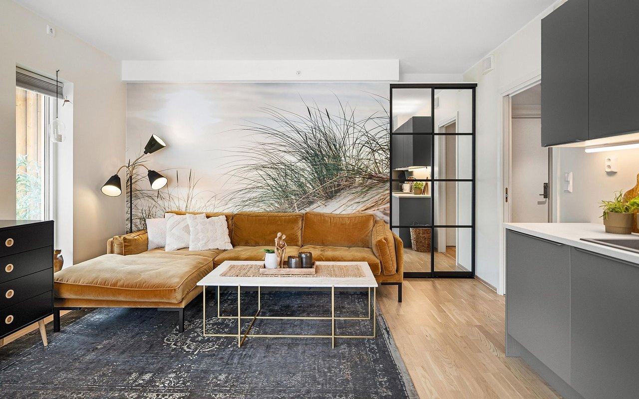 Living room with a caramel leather sectional, beach-grass mural, and black-framed glass partition.