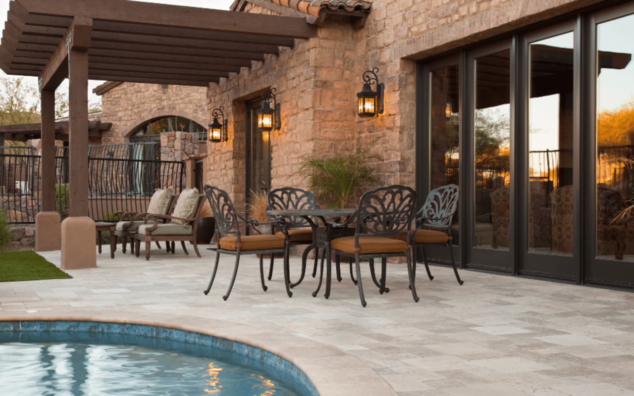 Stone patio with a timber pergola, outdoor dining furniture, and a pool beside the home.