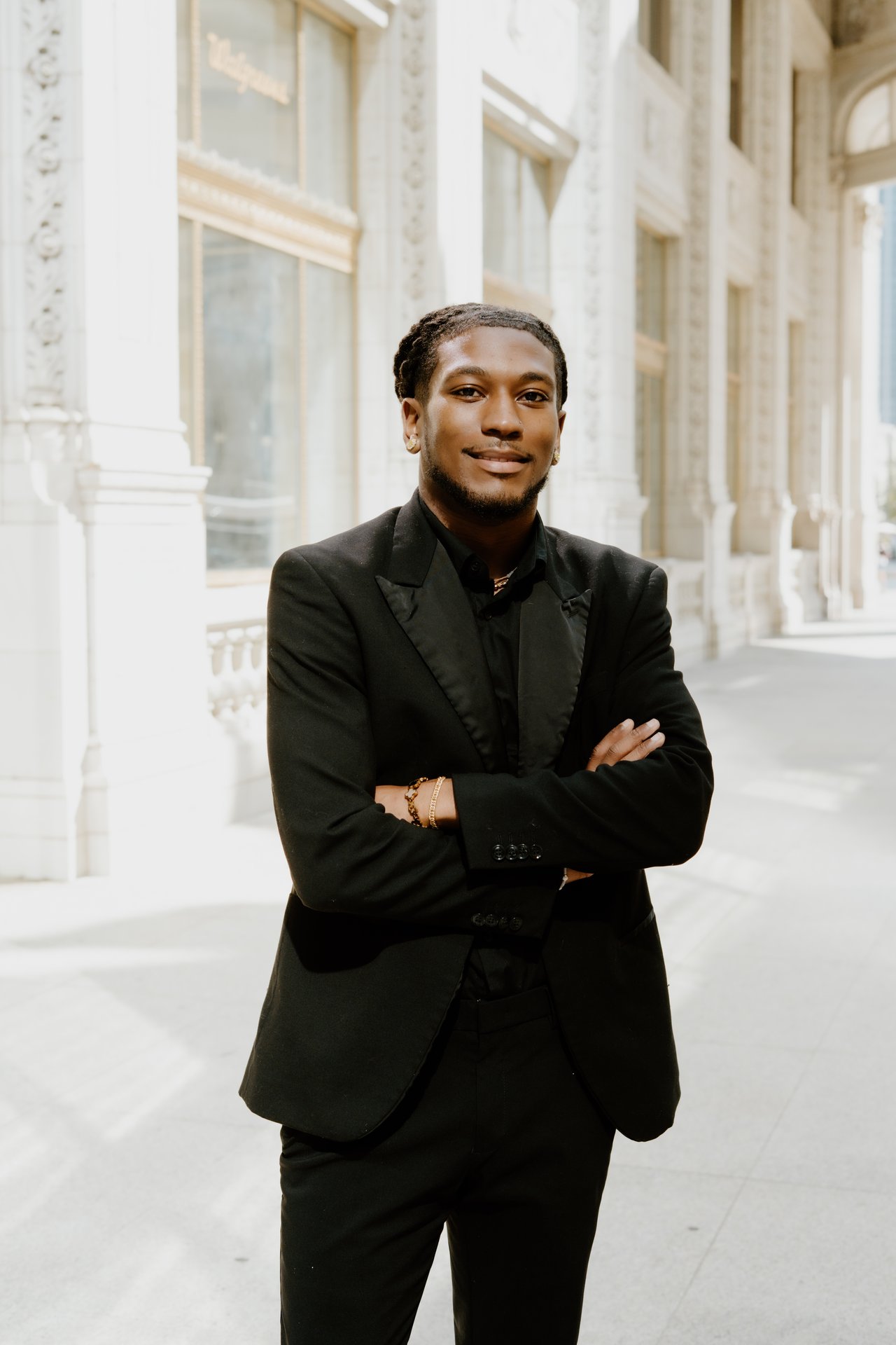 Romell Griffin in a black suit, standing with crossed arms outside an ornate stone building.
