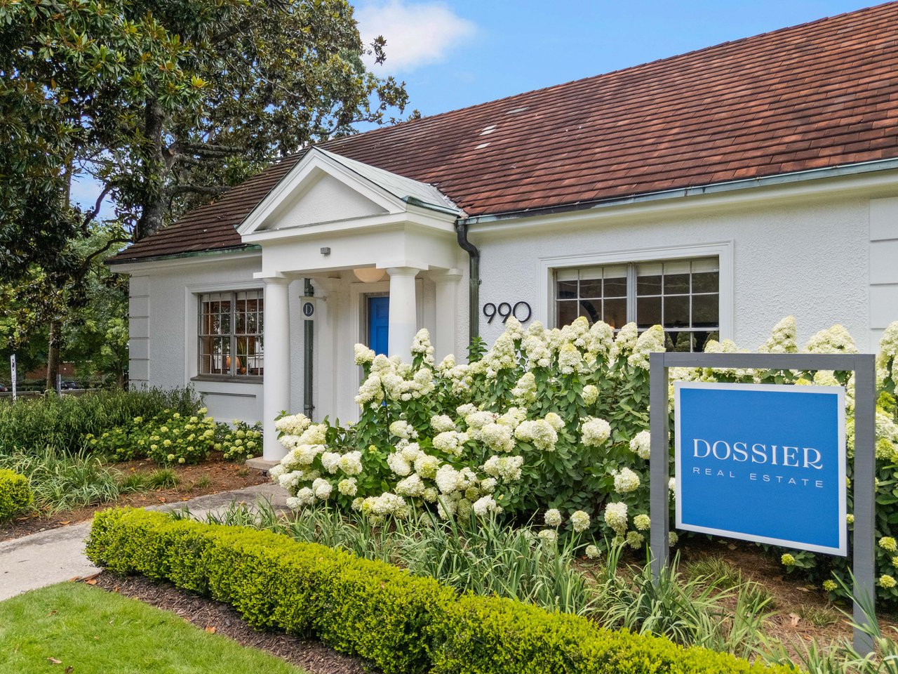 Dossier Real Estate office with a blue door and white hydrangeas along the front.