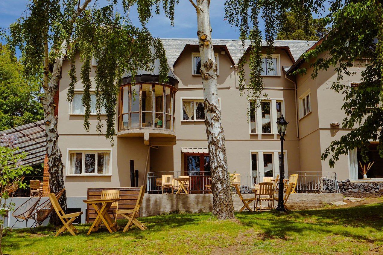 Boutique hotel exterior framed by birch trees, with a glass bay window and wooden patio seating.