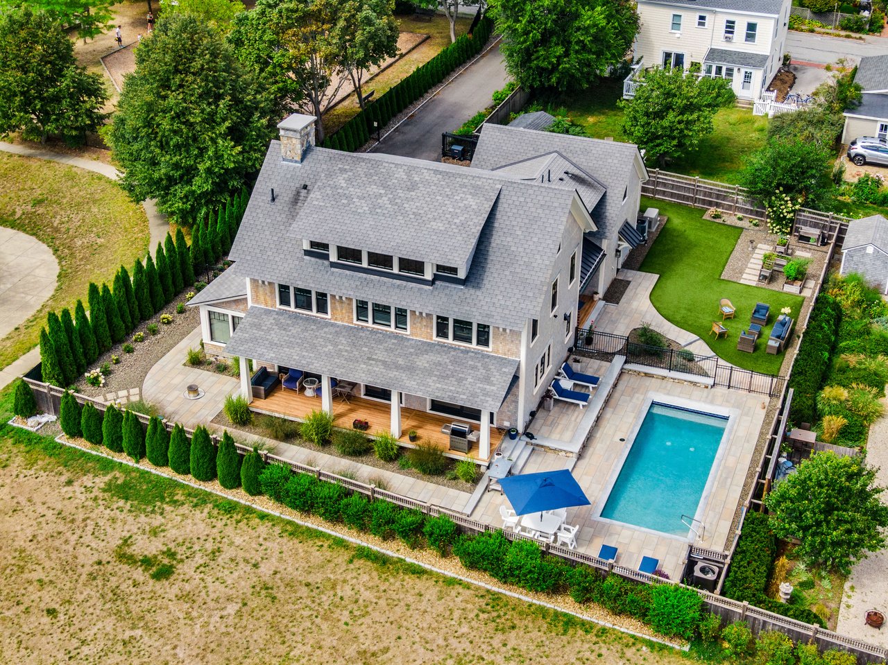 Aerial view of a large home with a fenced pool, landscaped yard, and covered patio.
