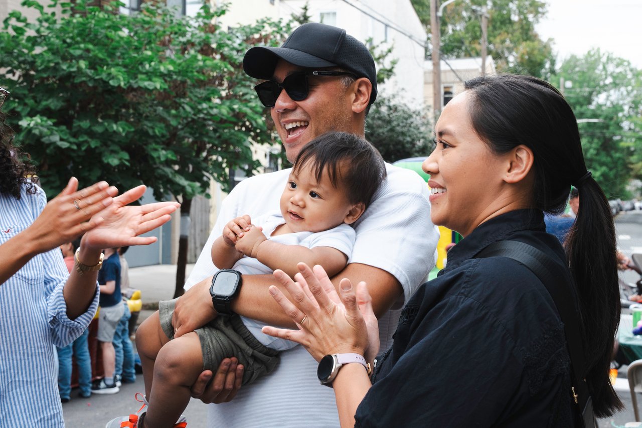 Neighbors chat at an outdoor gathering as a man holds a baby.
