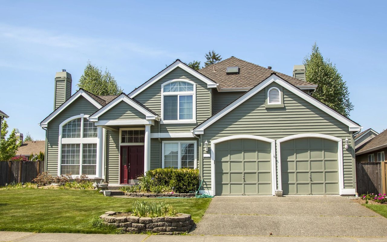 Gray-green two-story house with a red front door, twin garage doors, and landscaped front yard.