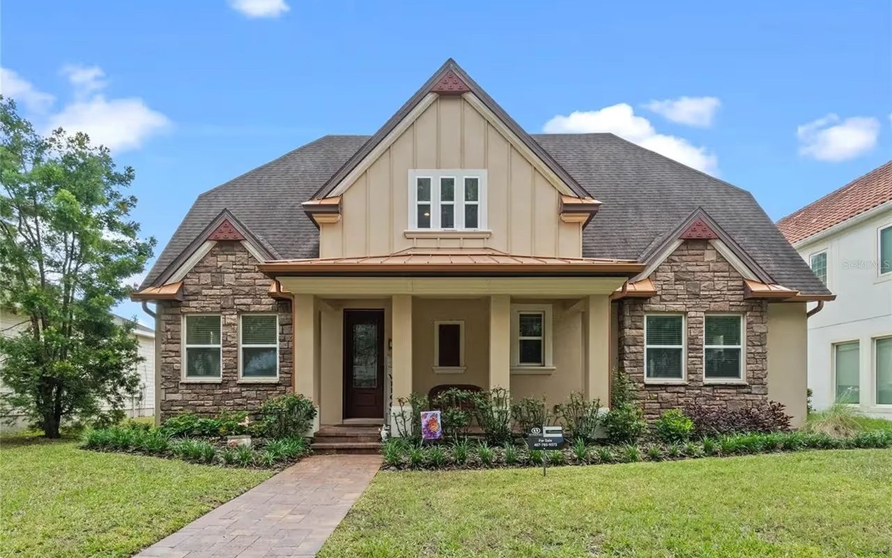 Two-story tan home with stone accents, a covered porch, and a paved front walkway.