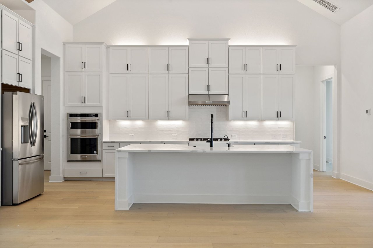 Chef's kitchen with a quartz waterfall island, Shaker-style cabinetry, and stainless steel appliances in the Cortaro home at 133 Mataro Cove, Dripping Springs, Texas.
