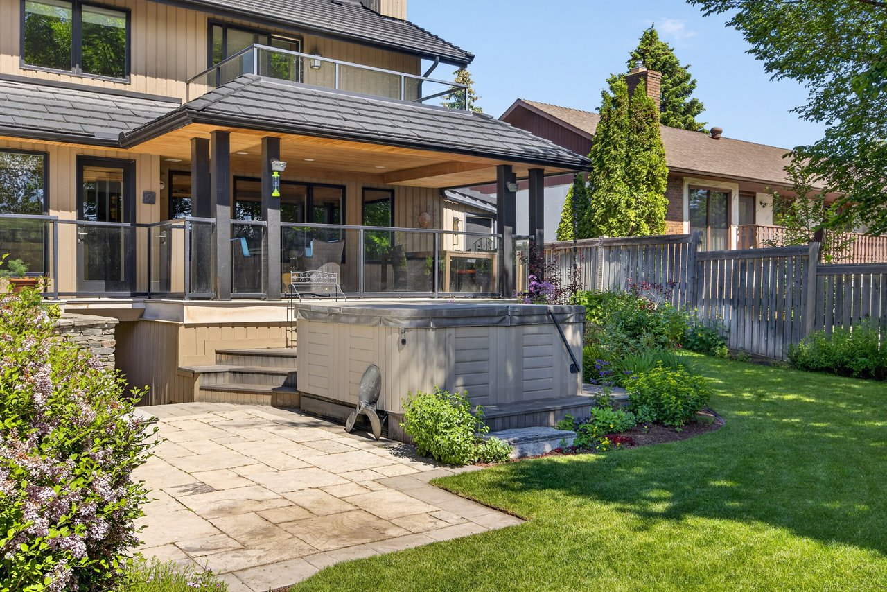Home’s covered rear deck overlooks a hot tub, stone patio, and landscaped lawn.