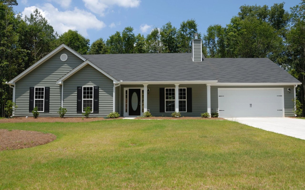 Gray single-story home with black shutters, covered entry, and attached white garage.