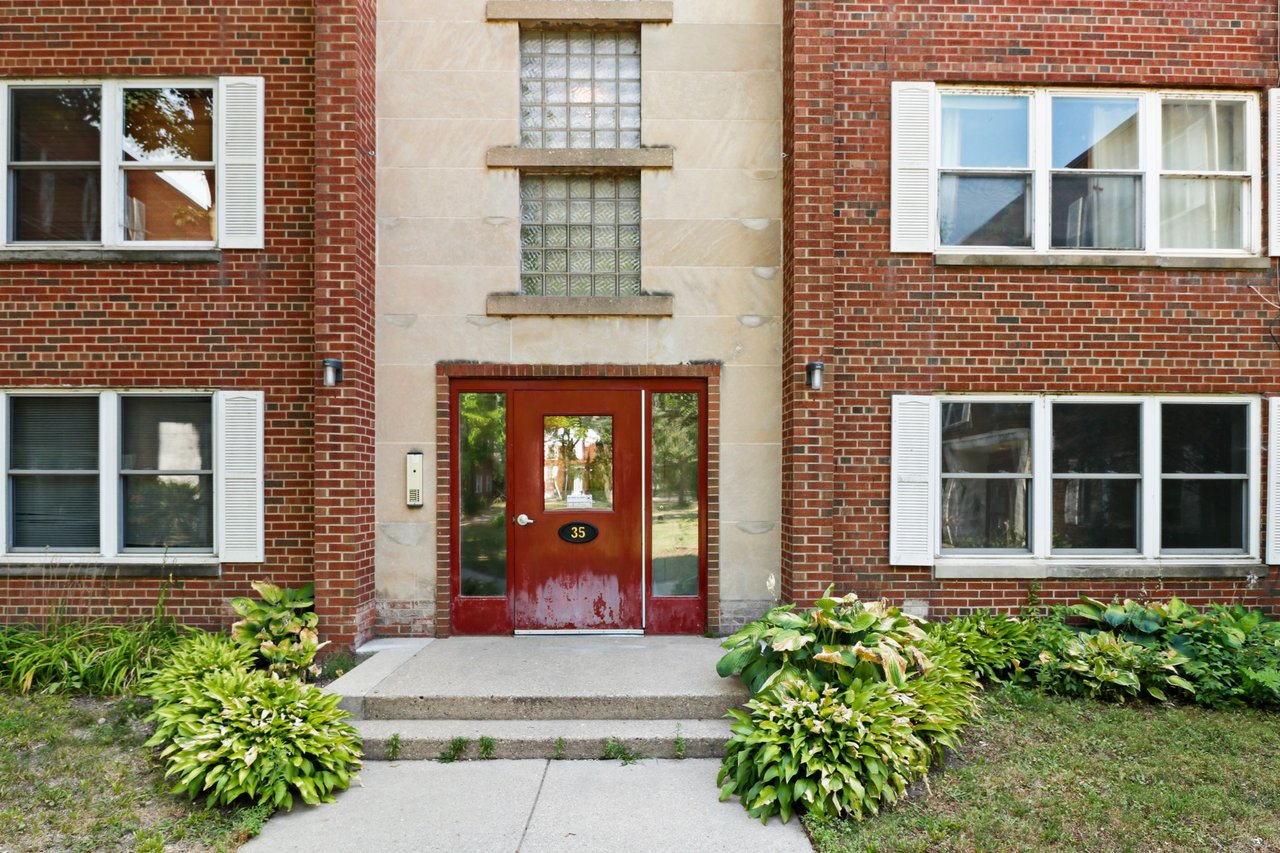Exterior of the condo building at 35 Sherman Terrace in Madison, showing the shared red entrance door, brick facade, white shutters, and landscaping.