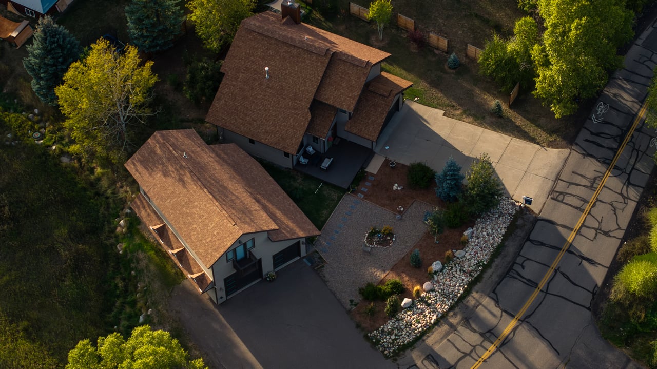 Aerial view of two homes with brown roofs, adjoining driveways, and a landscaped gravel yard.