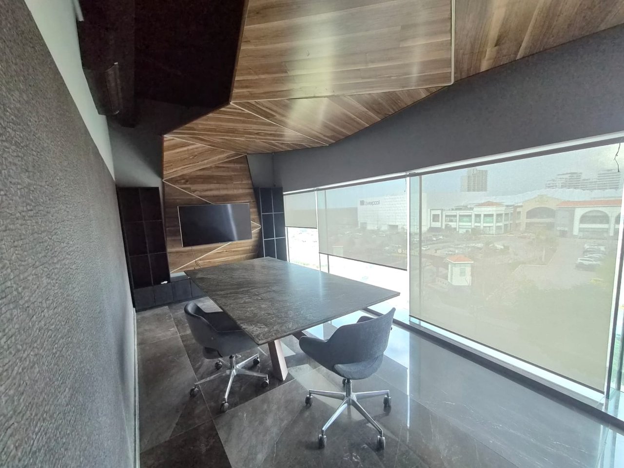 Modern office meeting room with a stone conference table, swivel chairs, and large windows.