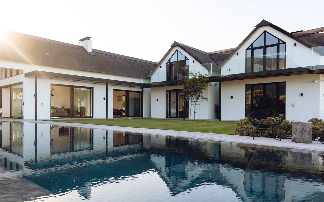 Modern white house with glass balconies and a swimming pool in the foreground.