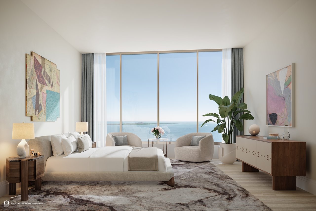 Furnished bedroom with a king bed and sitting area overlooking the water through floor-to-ceiling windows.
