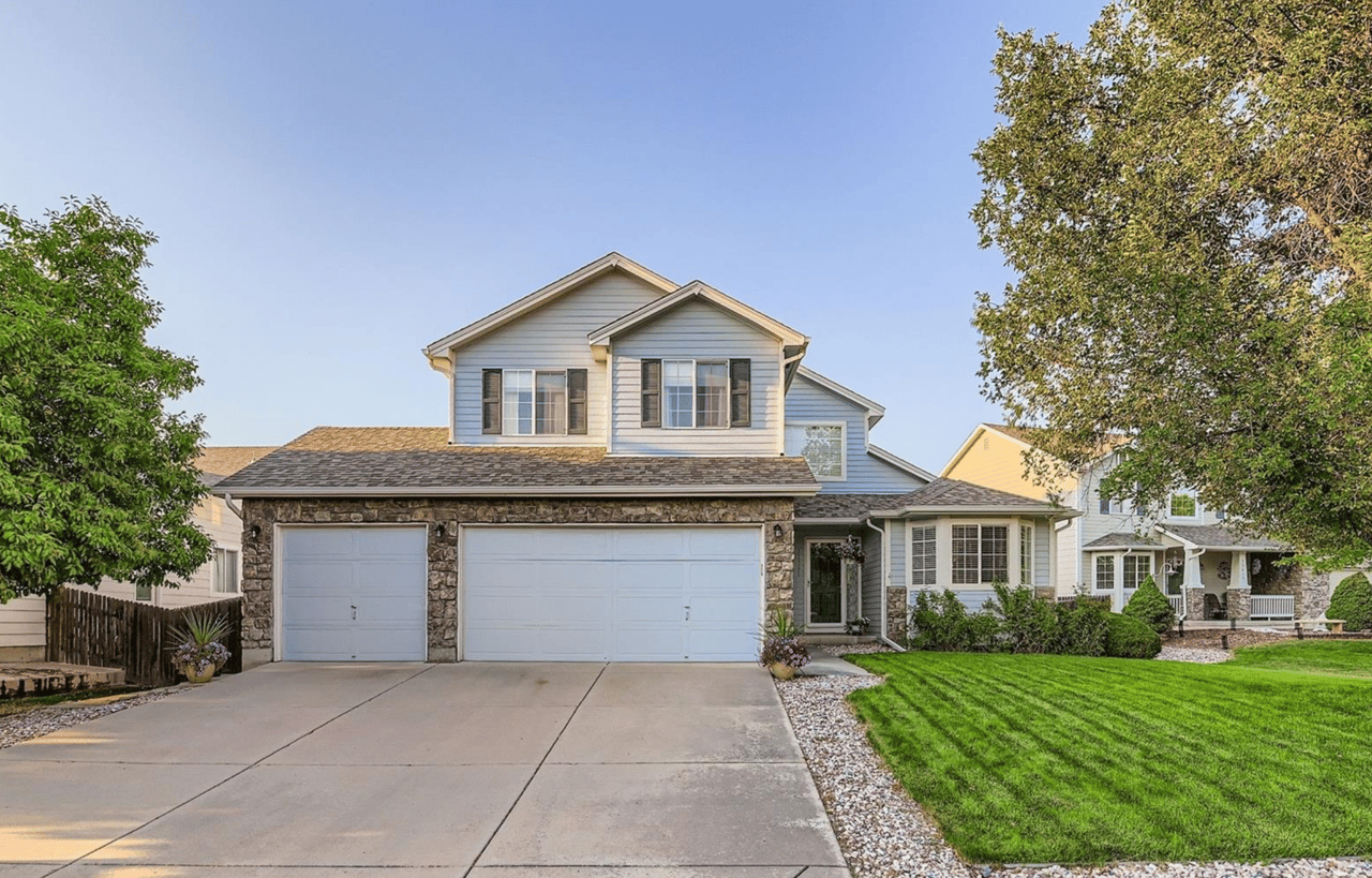 Two-story blue-sided house with stone accents, a double garage, wide driveway, and neatly mowed lawn.