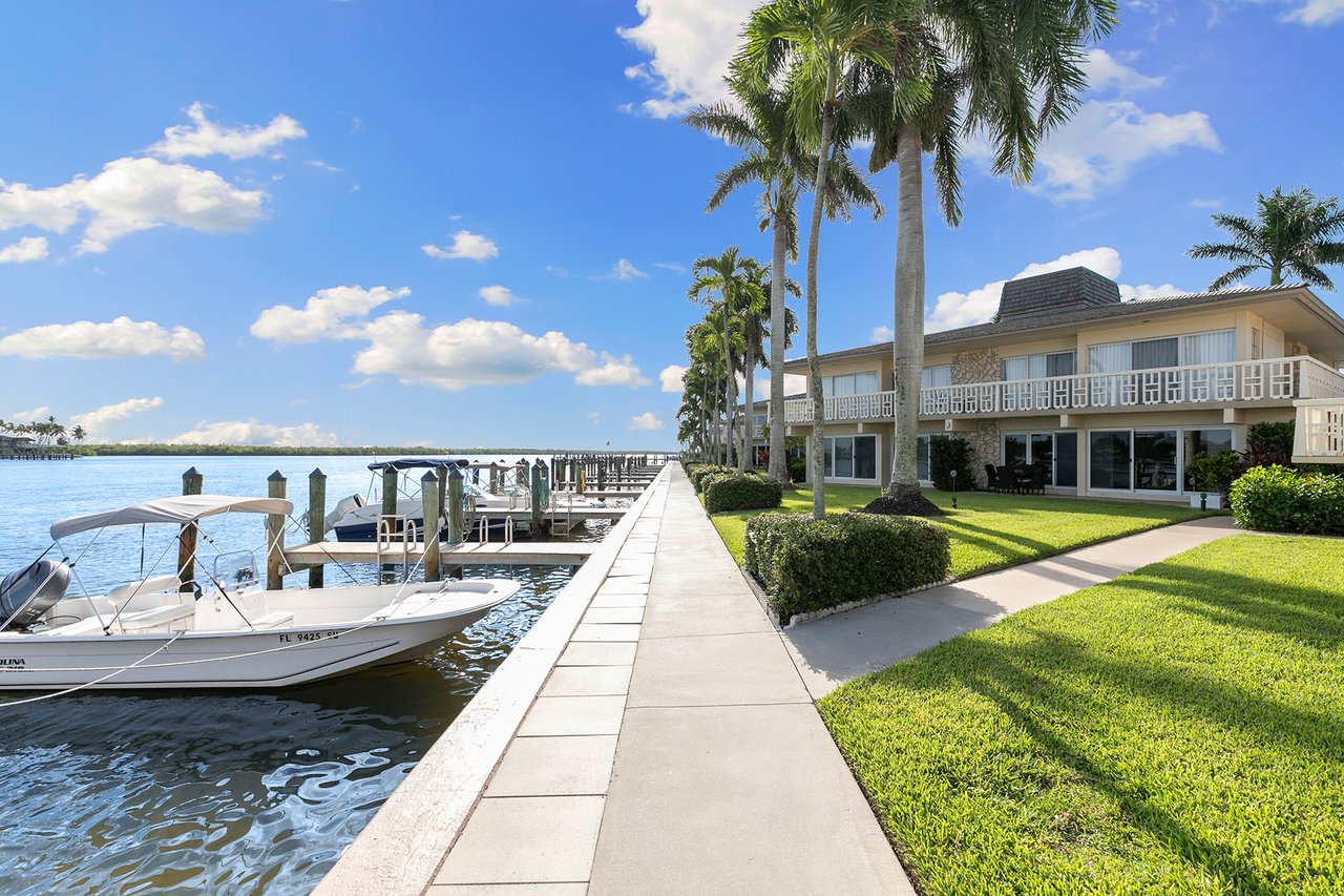 Waterfront condominium with palm trees, boats at the dock, and a waterside walkway.