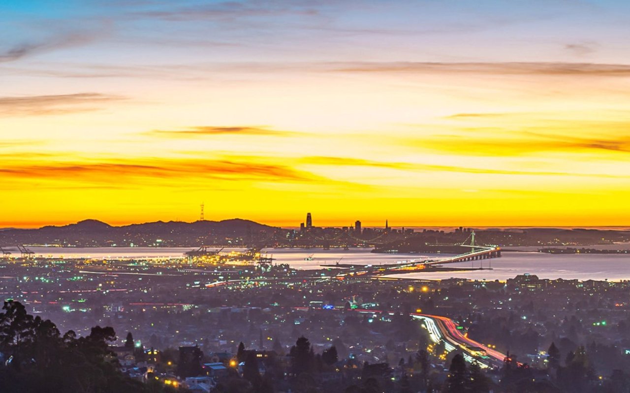 San Francisco Bay Bridge and skyline at dusk, seen across the East Bay beneath a glowing sunset.