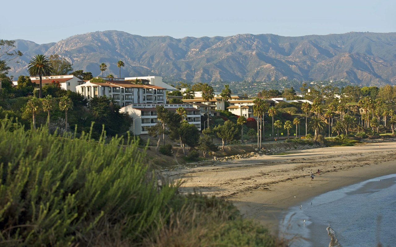 Santa Barbara coastline with beachfront buildings, palm trees, and mountains in the distance.
