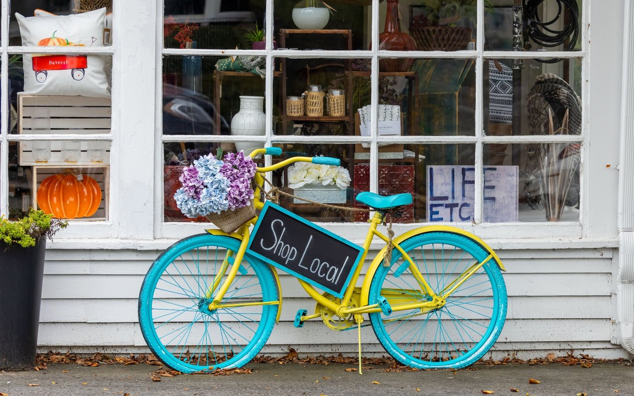 Yellow bicycle with turquoise wheels and a “Shop Local” sign outside a gift shop.