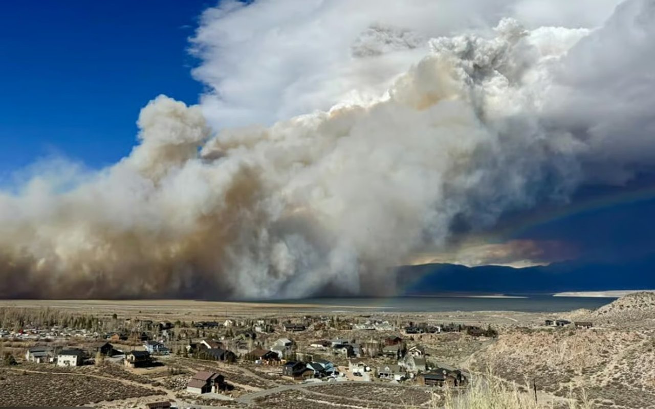 Wildfire smoke billows over a small settlement in a dry valley.
