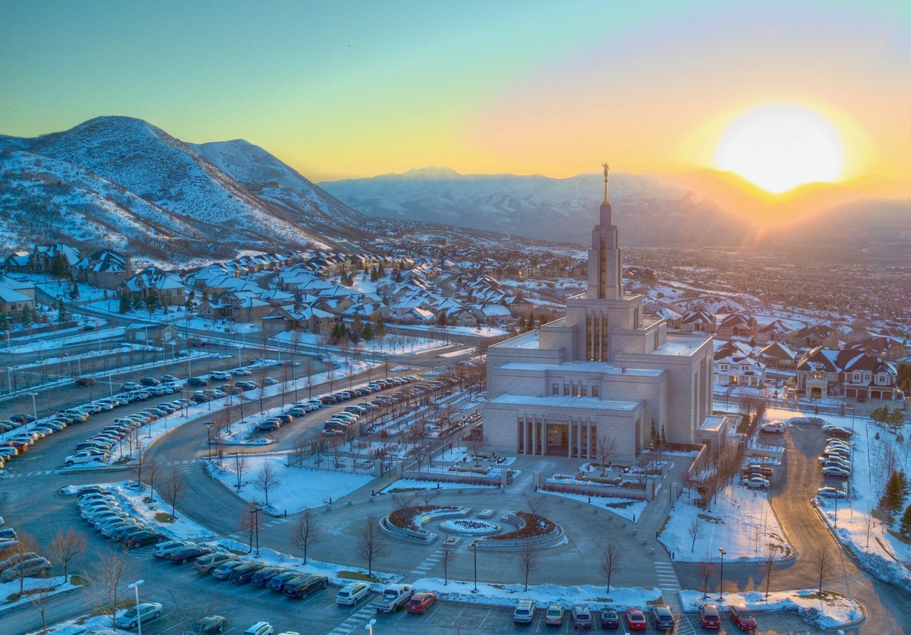 Snow-covered Utah neighborhood and temple beneath the Wasatch Mountains at sunset.