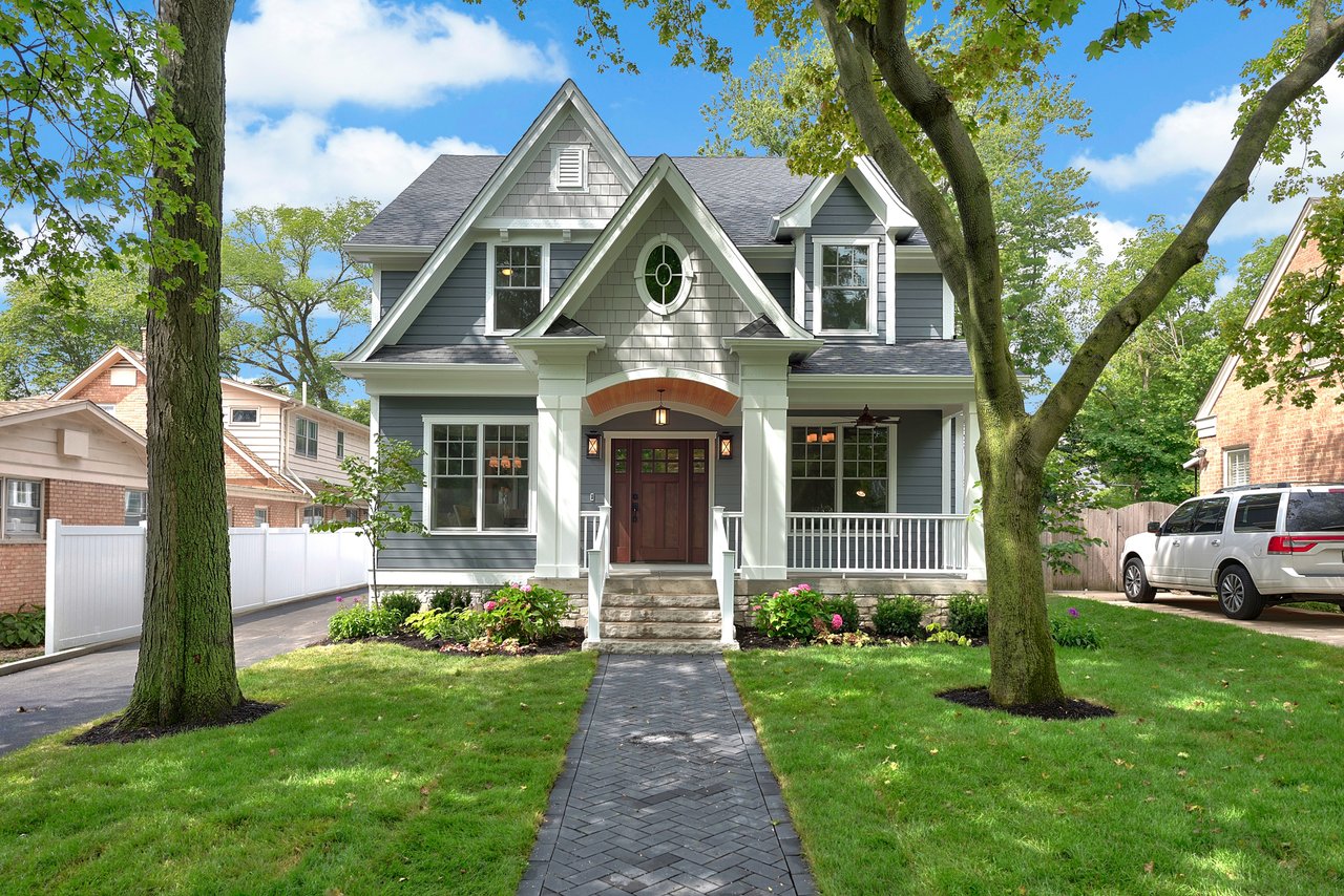 Gray two-story home with a gabled roof, covered porch, brick entry arch, and tree-lined walkway.