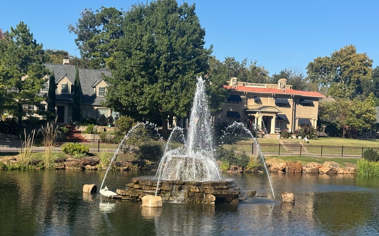 Neighborhood pond fountain with homes and mature trees behind it.