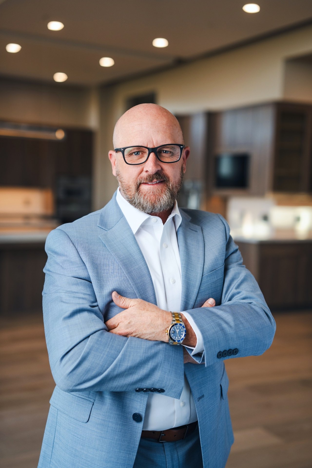 Scott Silva in a light blue suit and glasses, standing with his arms crossed indoors.