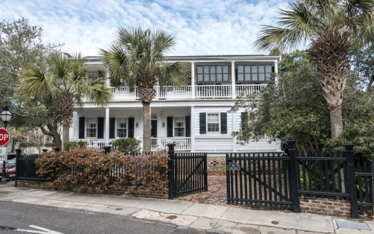 White Charleston home with two covered porches, dark shutters, and a black iron fence.