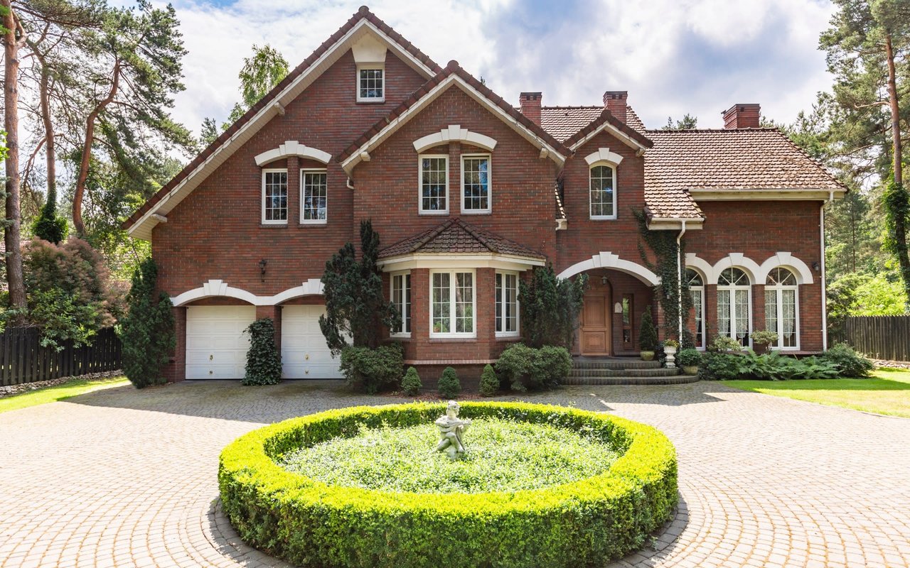 Red-brick home with two garages and a circular hedge garden surrounding a fountain.