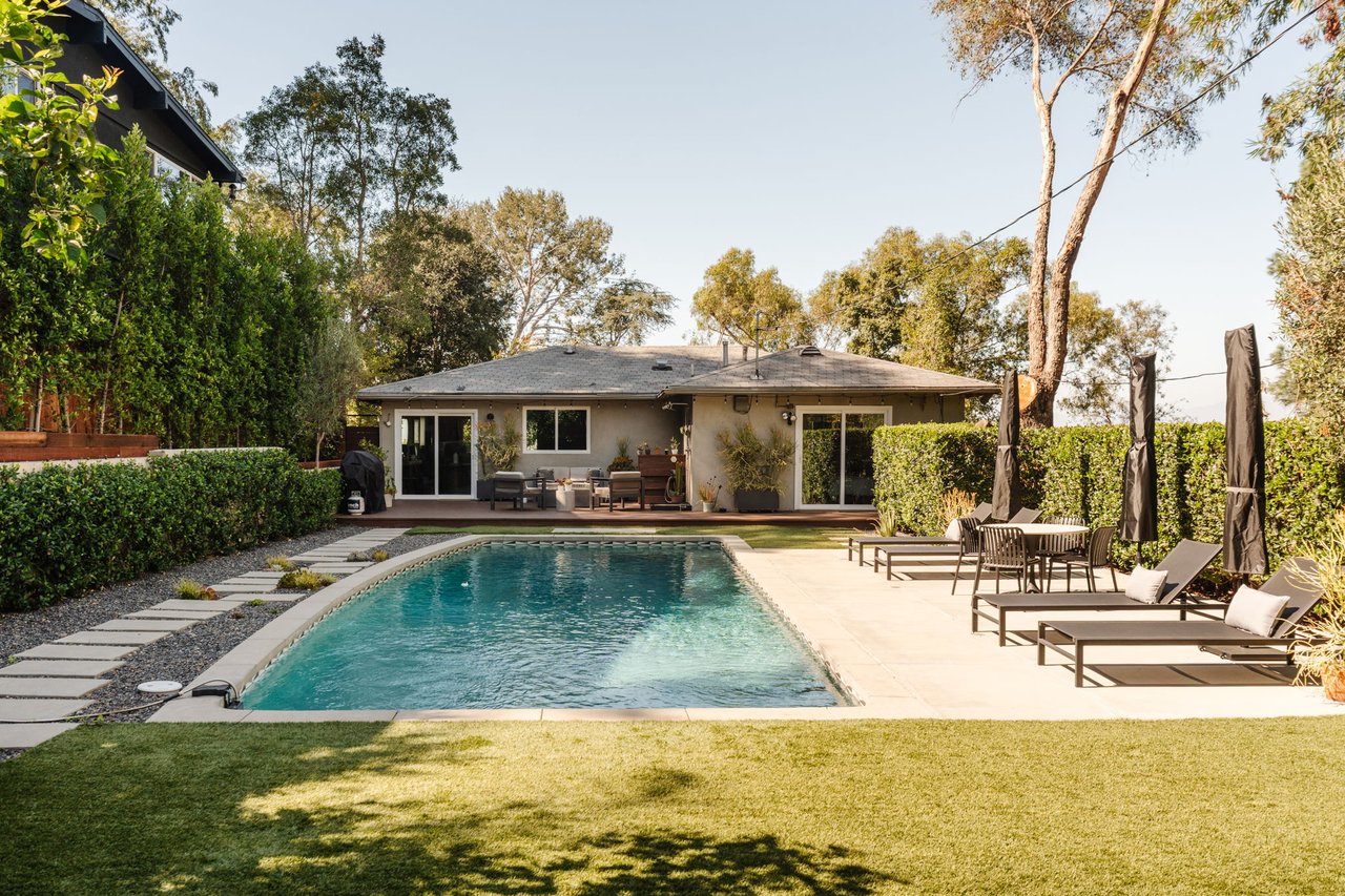 Backyard pool in front of a single-story home, with patio seating and a lawn.