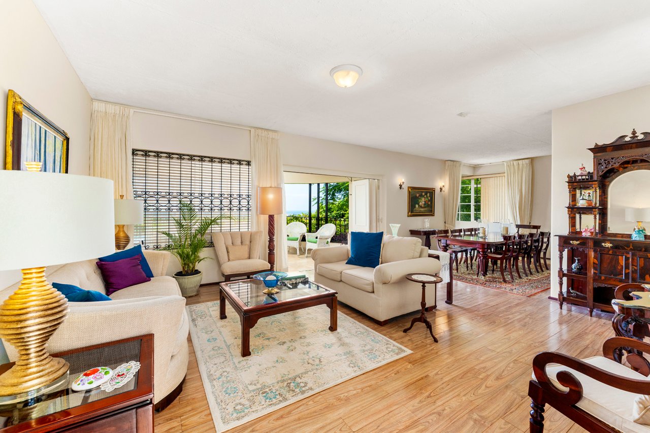Furnished living and dining room with cream sofas, polished wood floors, and a glimpse of the sea through the windows.