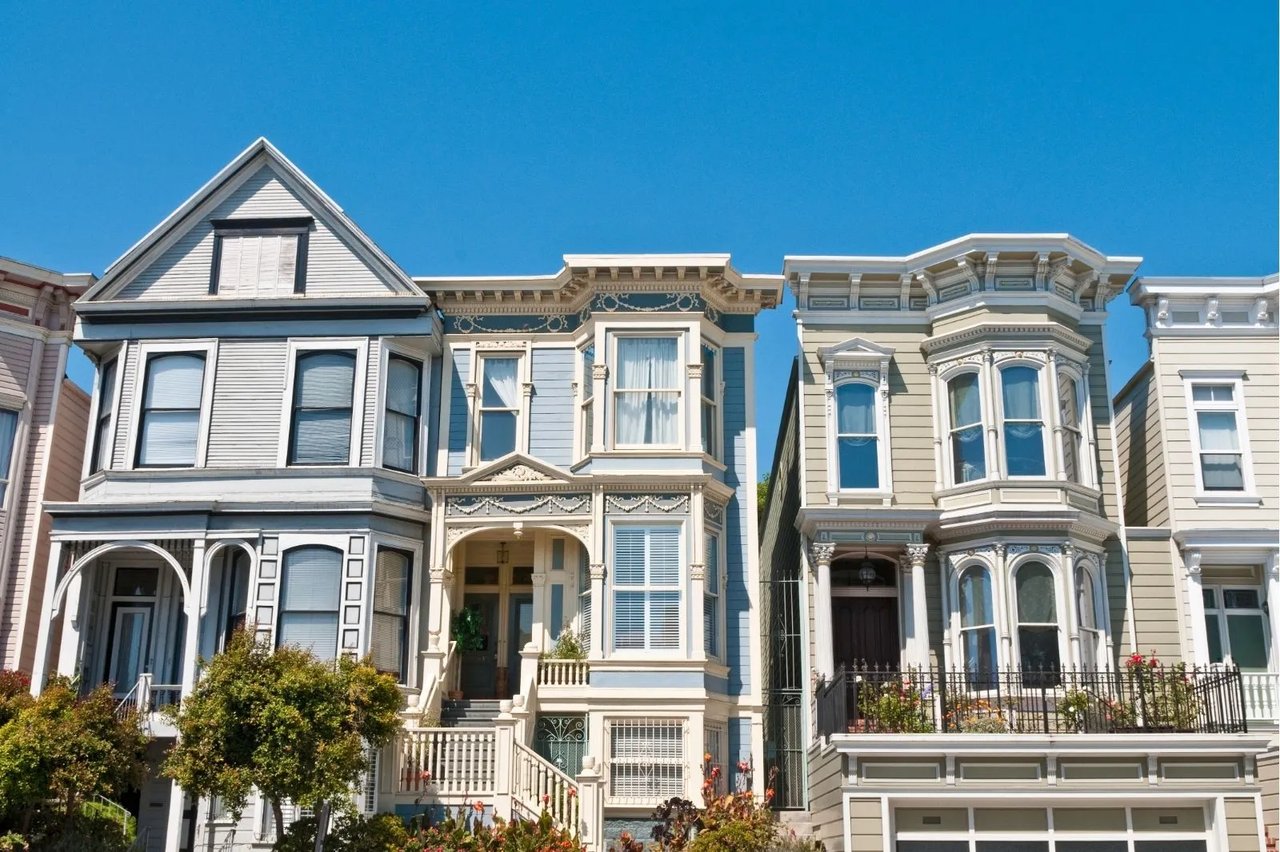Row of restored Victorian homes in Pacific Heights, San Francisco, with Italianate bay windows, ornate cornices, and soft gray, blue, and sage exteriors under a clear blue sky.
