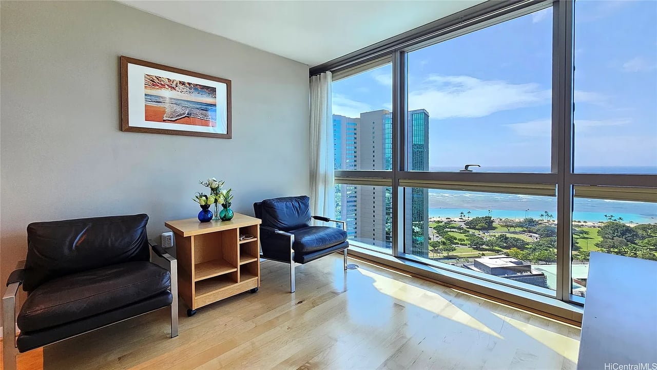 Furnished living area with leather chairs and floor-to-ceiling windows overlooking the ocean and shoreline.