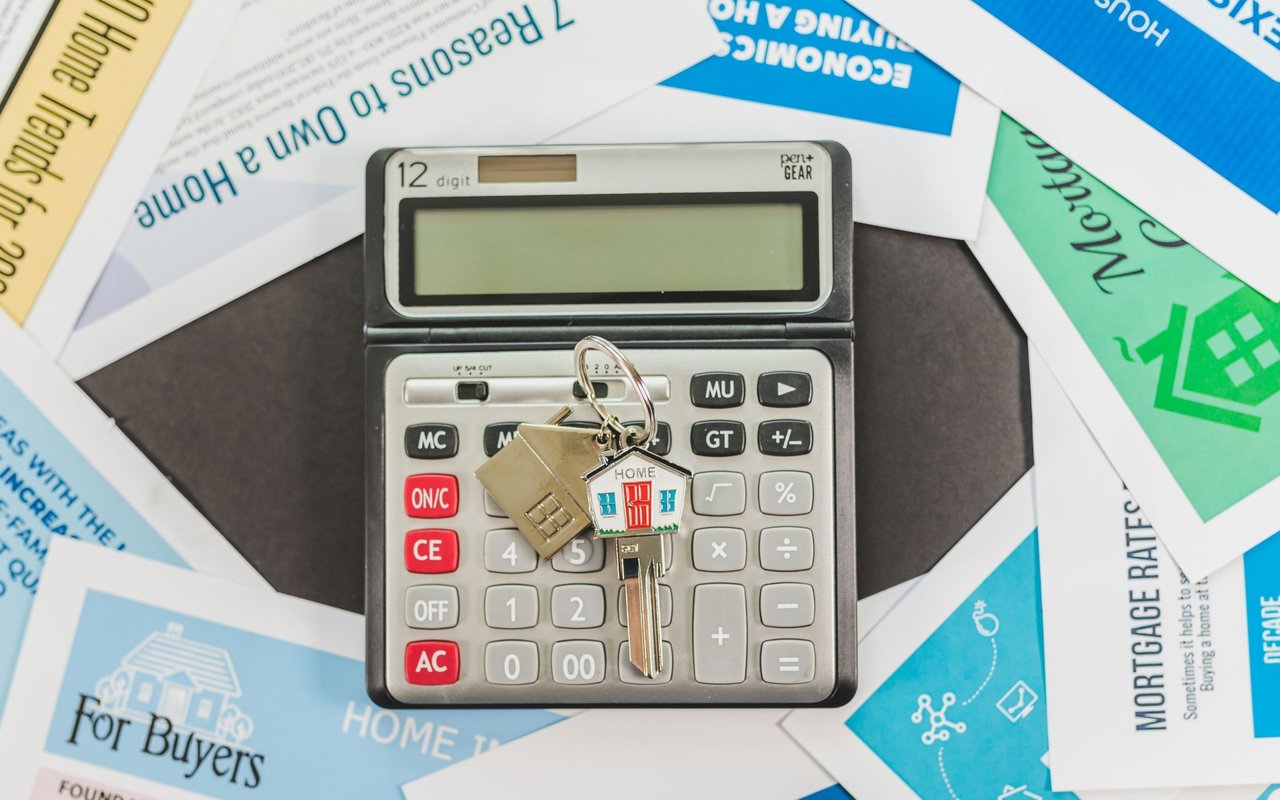 Calculator with house keys and a house-shaped keychain on mortgage and home-buying brochures.