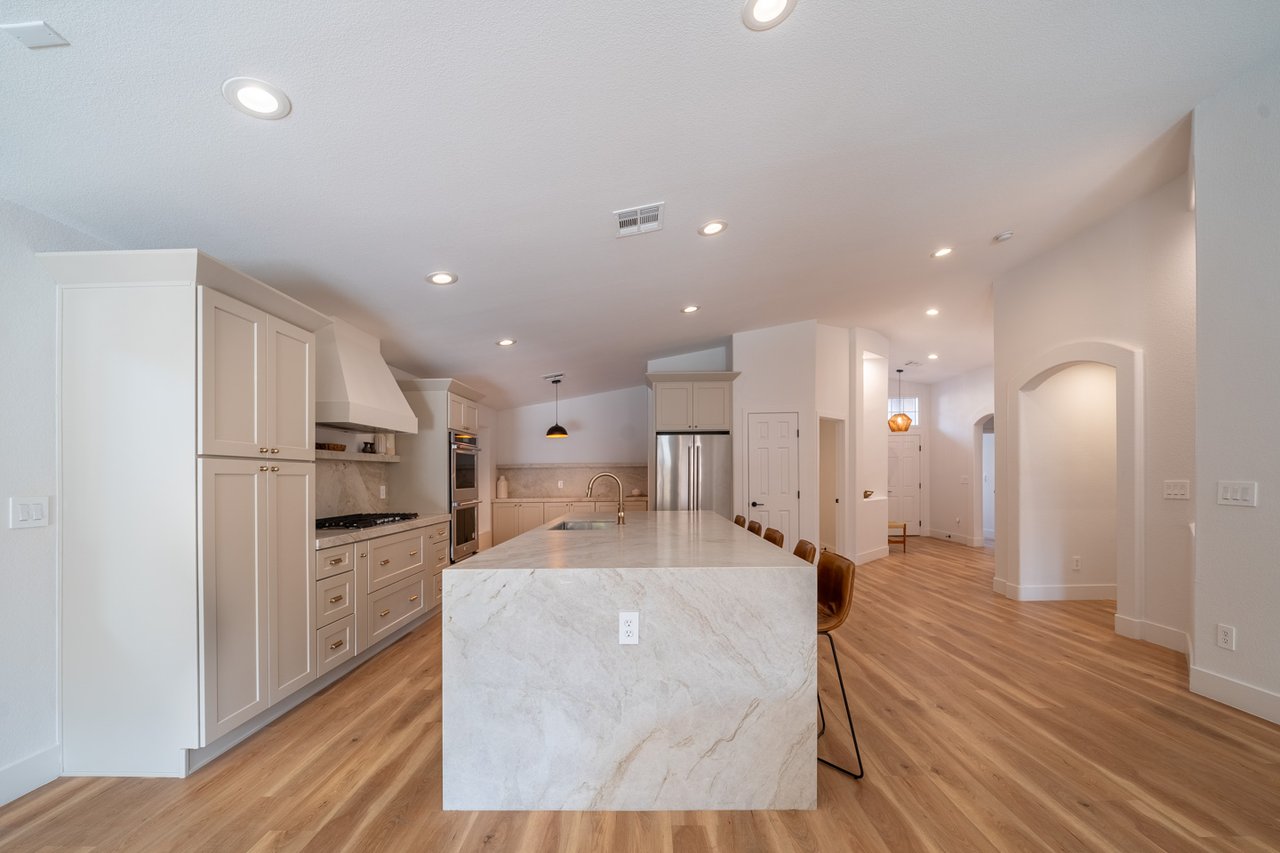 Kitchen with a large marble island, shaker cabinets, stainless-steel appliances, and wood flooring.