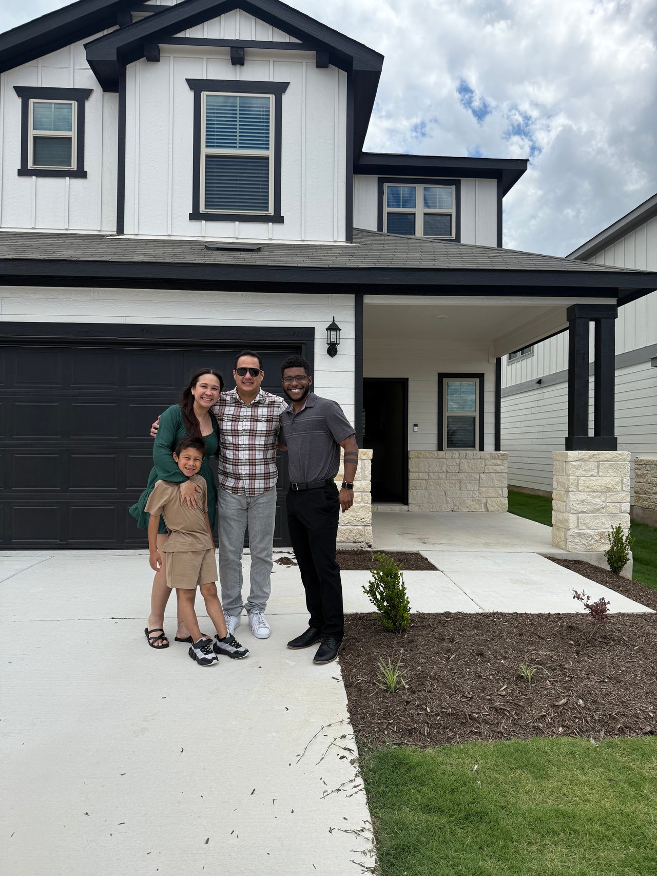 White two-story home with black trim and a covered entry, with a family and agent in the driveway.