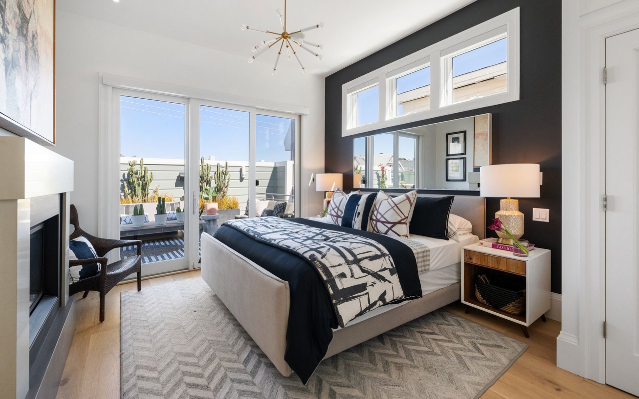 Staged bedroom with a charcoal accent wall, fireplace, and sliding doors to a terrace.