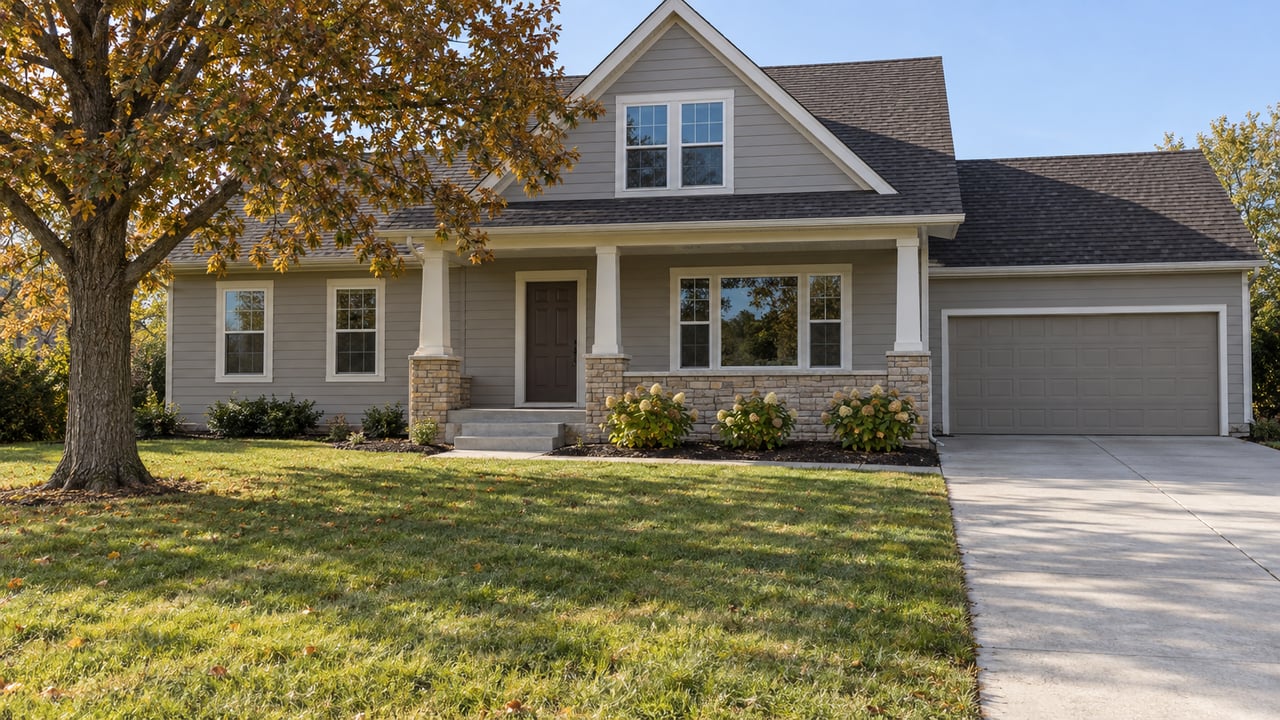 Traditional gray-sided home with a covered porch, generous lawn, mature oak and concrete driveway in clear autumn afternoon light.