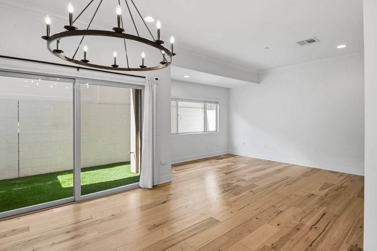 Spacious living room with circular iron chandelier, large sliding glass doors to private patio, and wide-plank hardwood floors