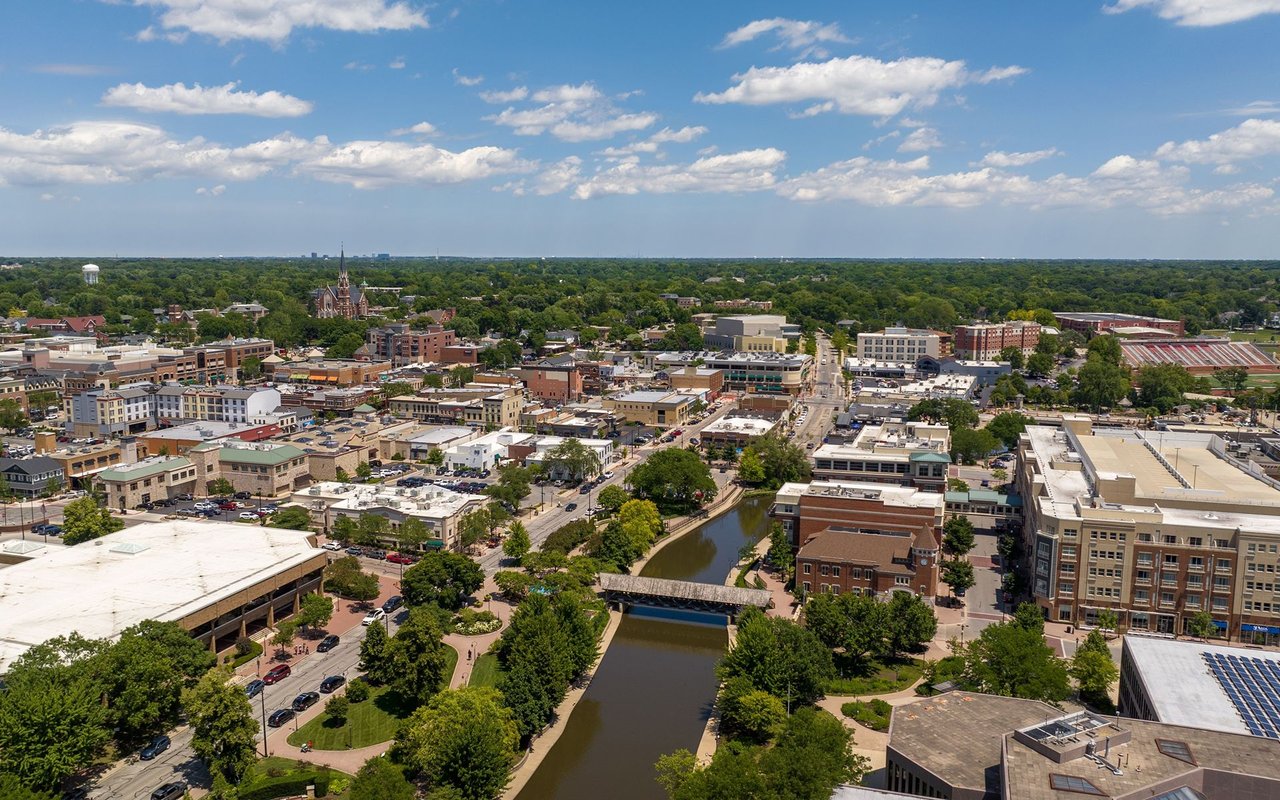 Aerial view of downtown Naperville and the riverwalk, with a pedestrian bridge and church steeple.
