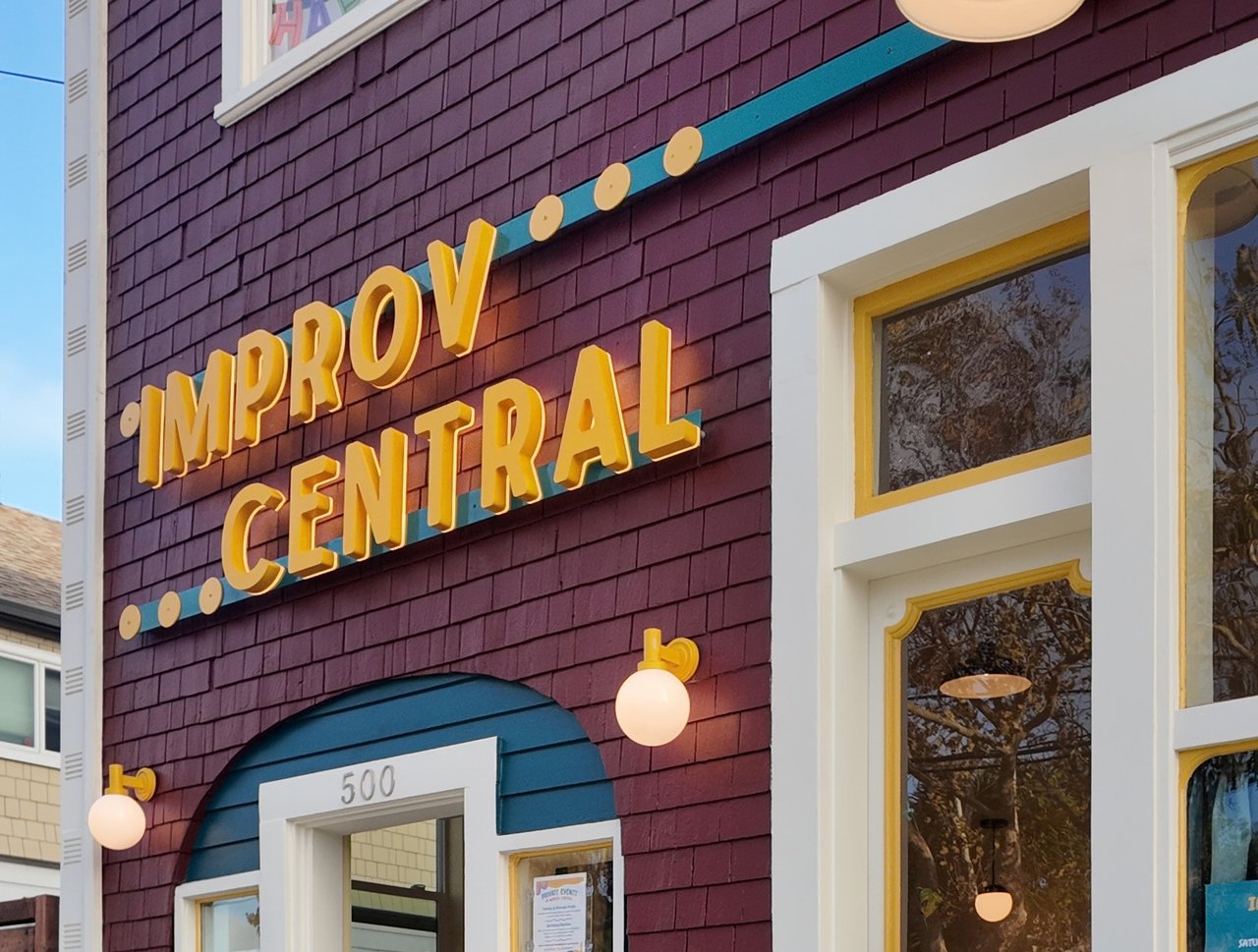 Improv Central storefront with plum shingles, teal trim, and yellow lettering.