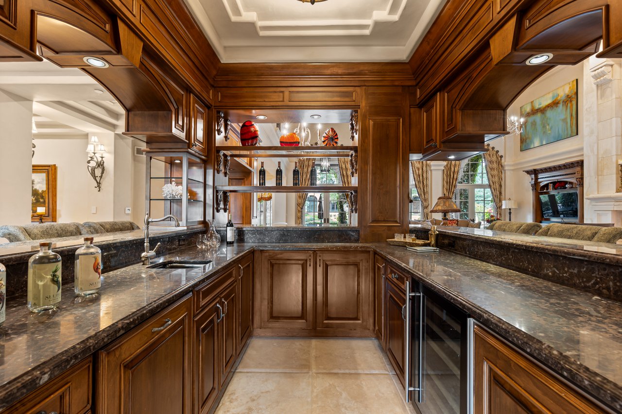 Home bar with dark wood cabinetry, polished stone counters, display shelves, and glass-front refrigerators.