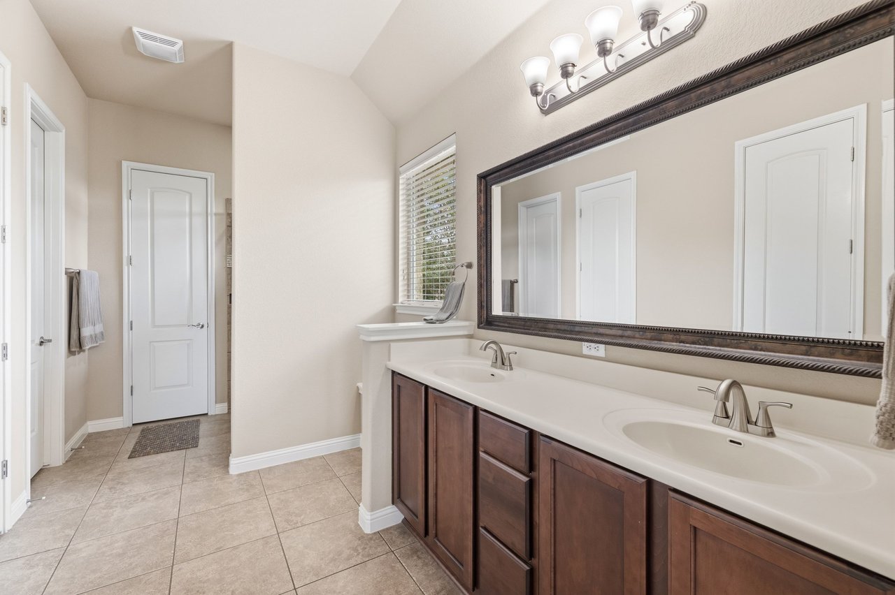 Bathroom with a double-sink vanity, dark wood cabinets, and a large framed mirror.