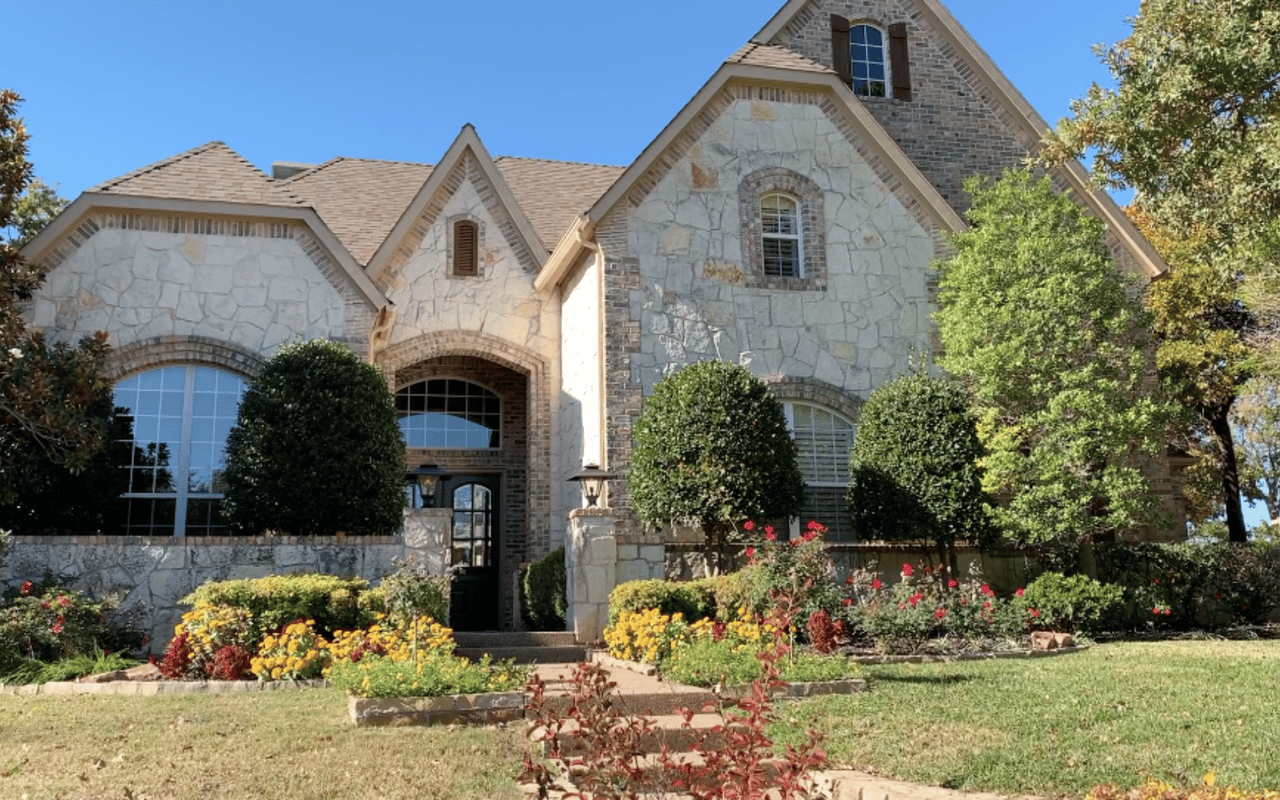 Two-story stone-and-brick house with a prominent gabled facade and colorful front garden.